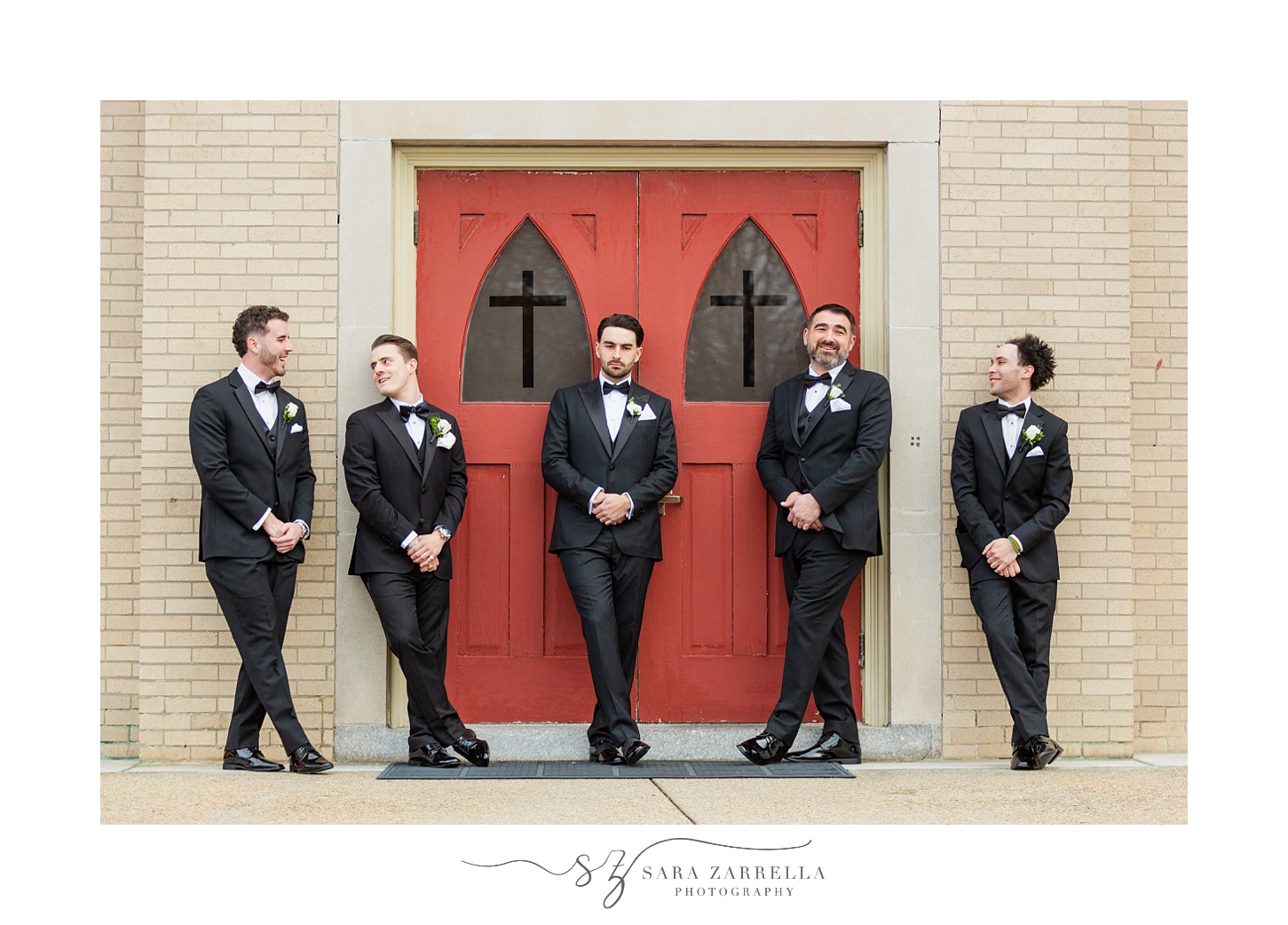 groomsmen lean against red door of St. Thomas in Providence RI