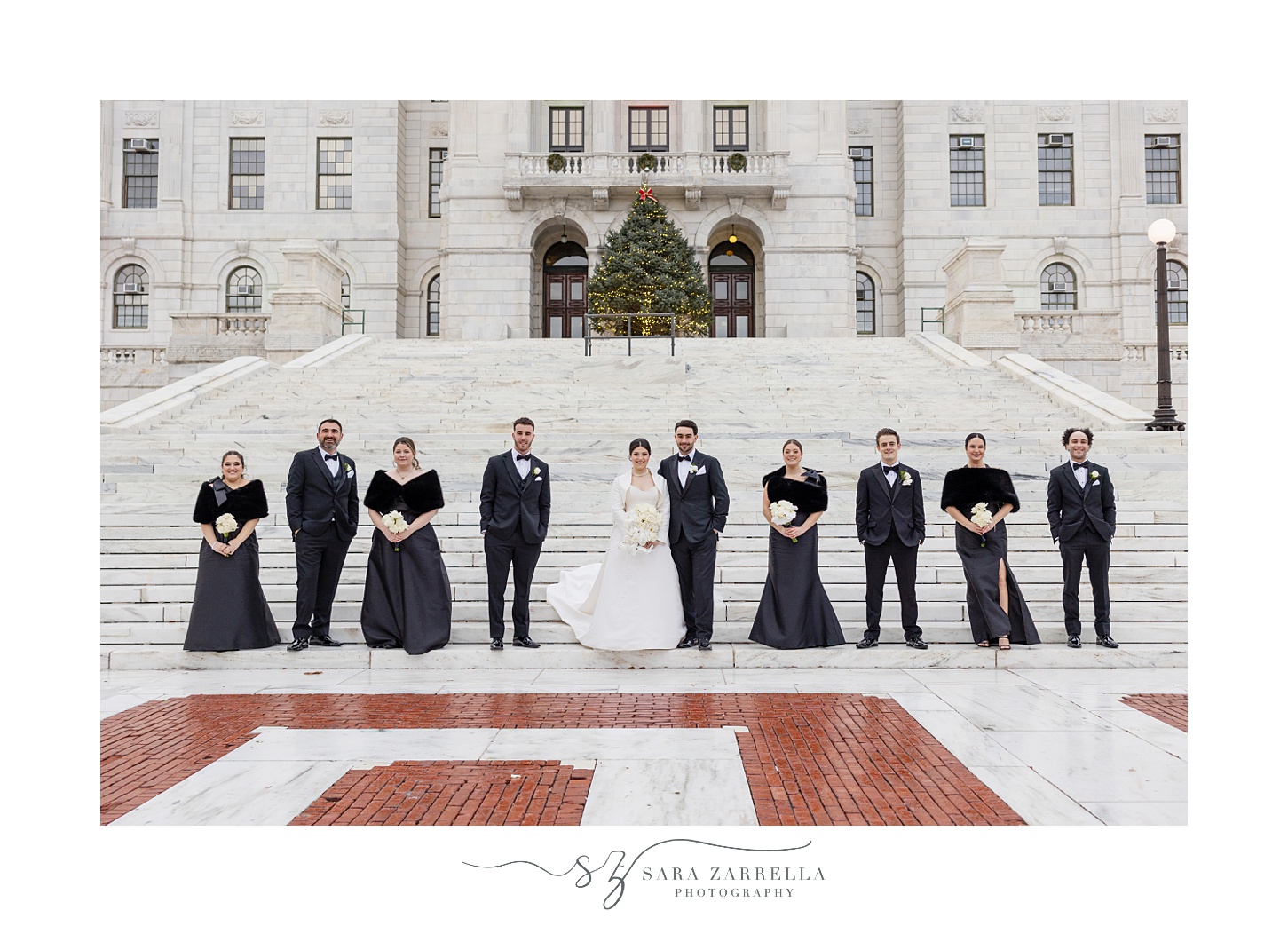 newlyweds hug with bridal party in black attire in a line near them at the RI State House