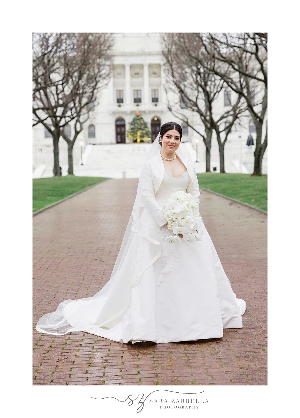 bride stands on brick pathway outside the RI State House with veil around her shoulders 