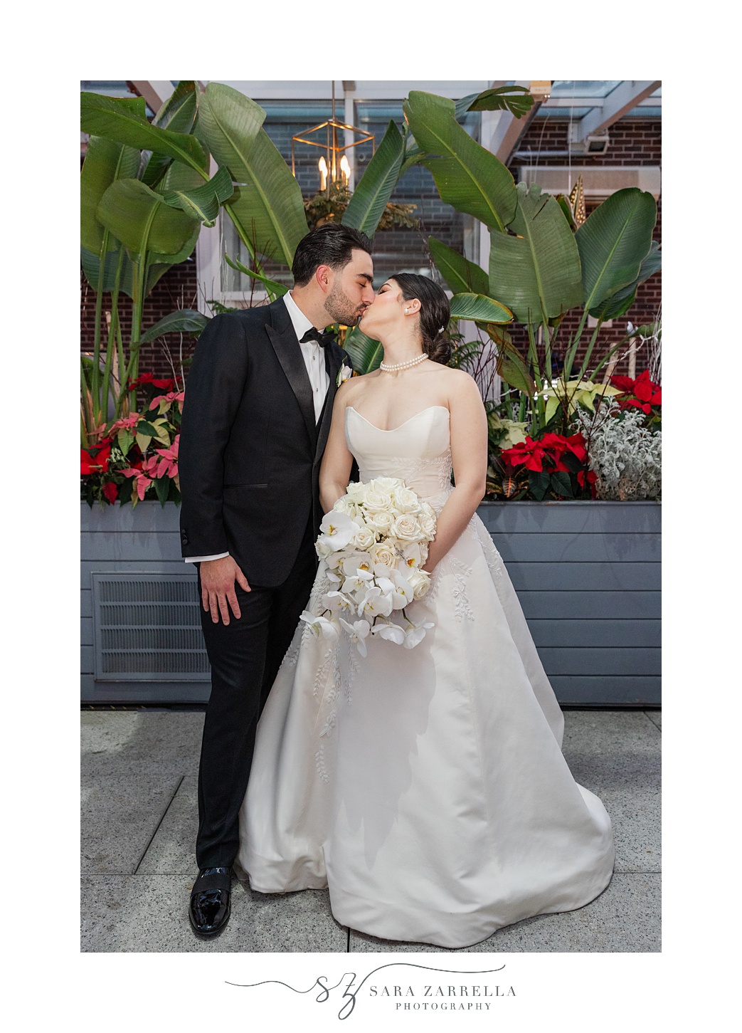 bride and groom kiss in front of flowers in walkway at ballroom at the Providence G