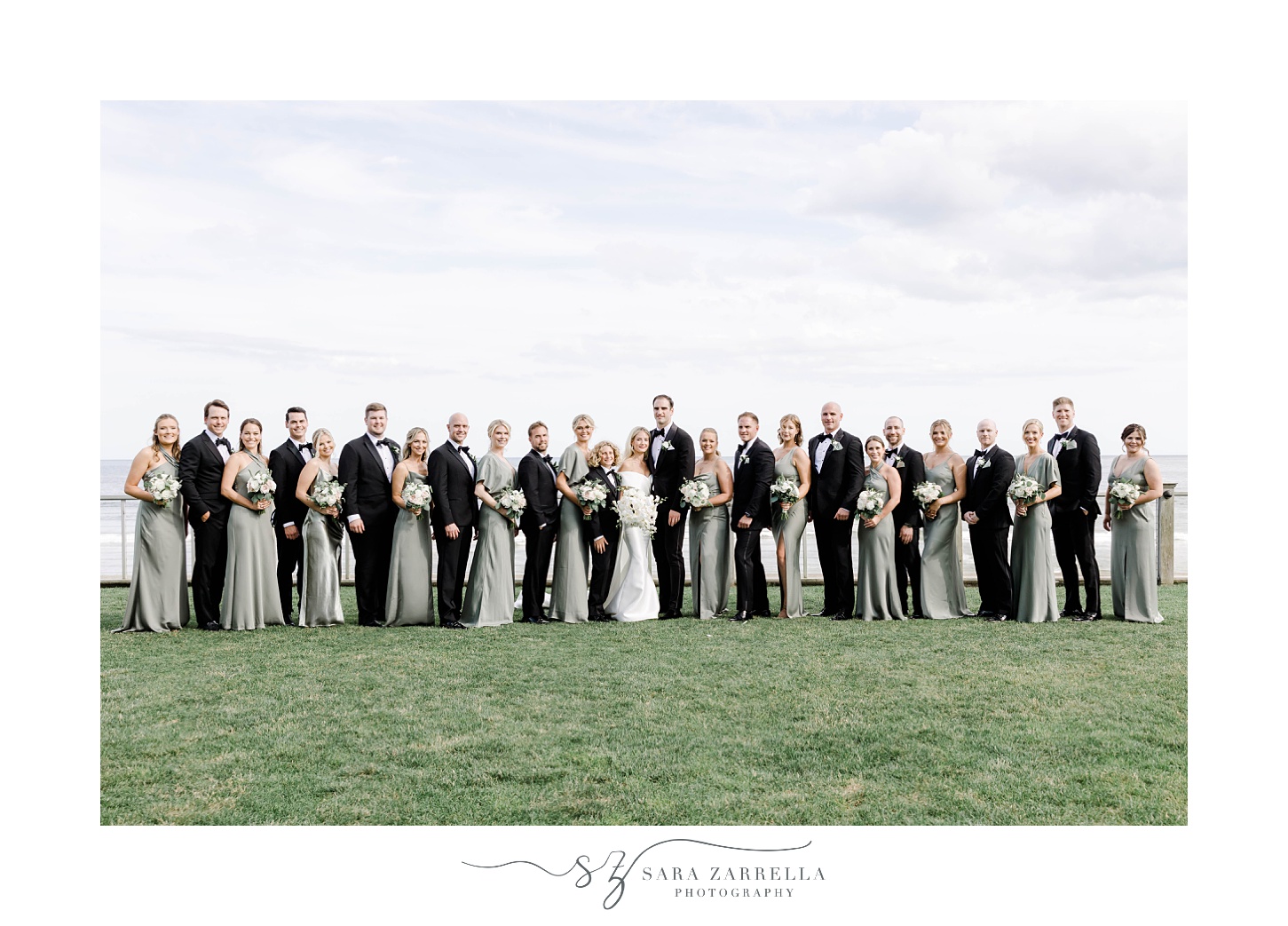 bride and groom pose with large wedding party in black suit with sage green gowns at the Dunes Club