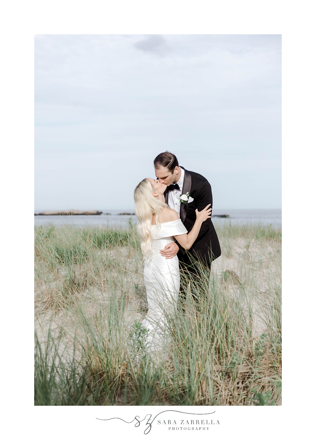 bride and groom kiss in tall grass near Narragansett Bay