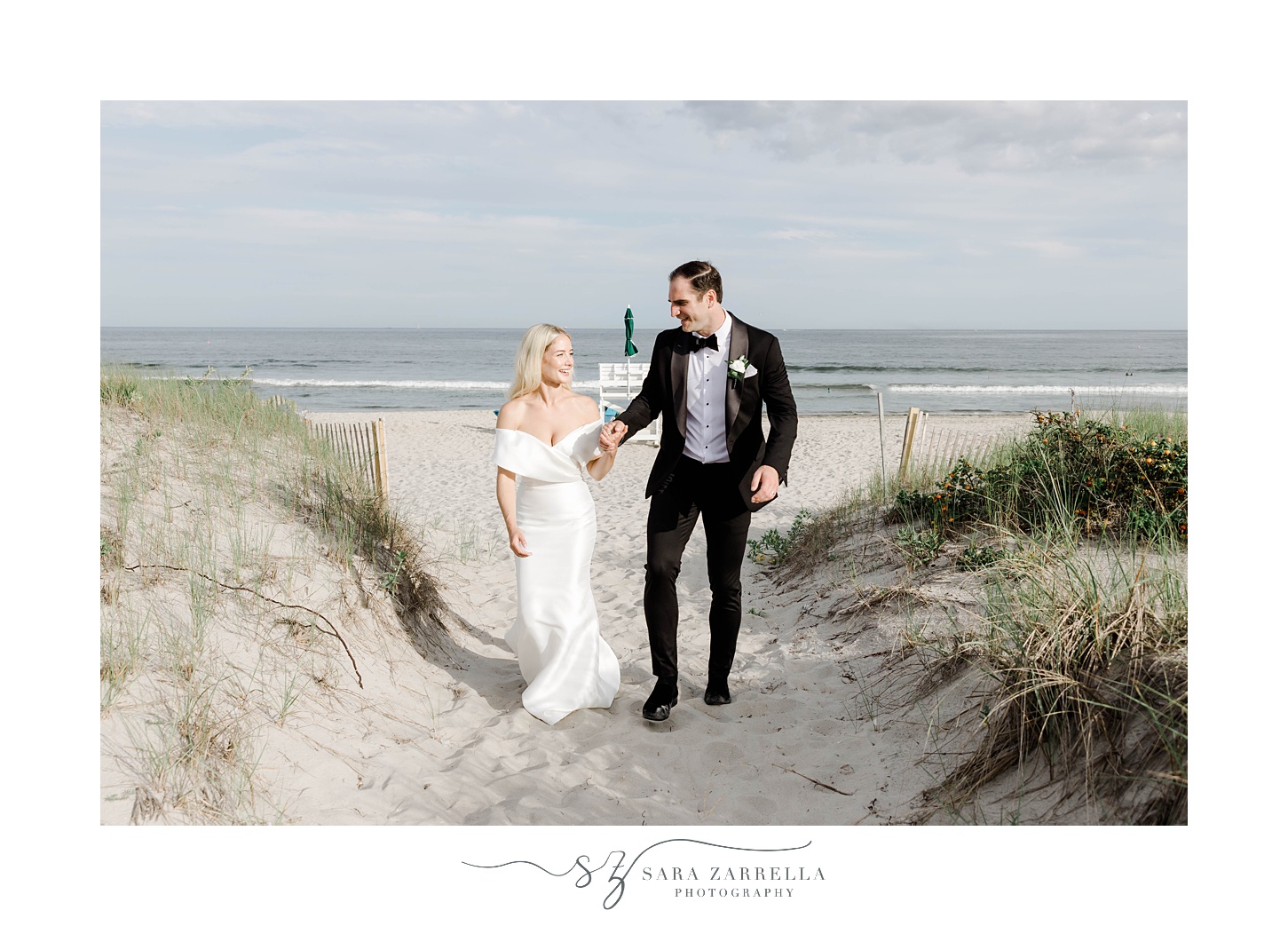 groom and bride walk up path on Narragansett Bay beach