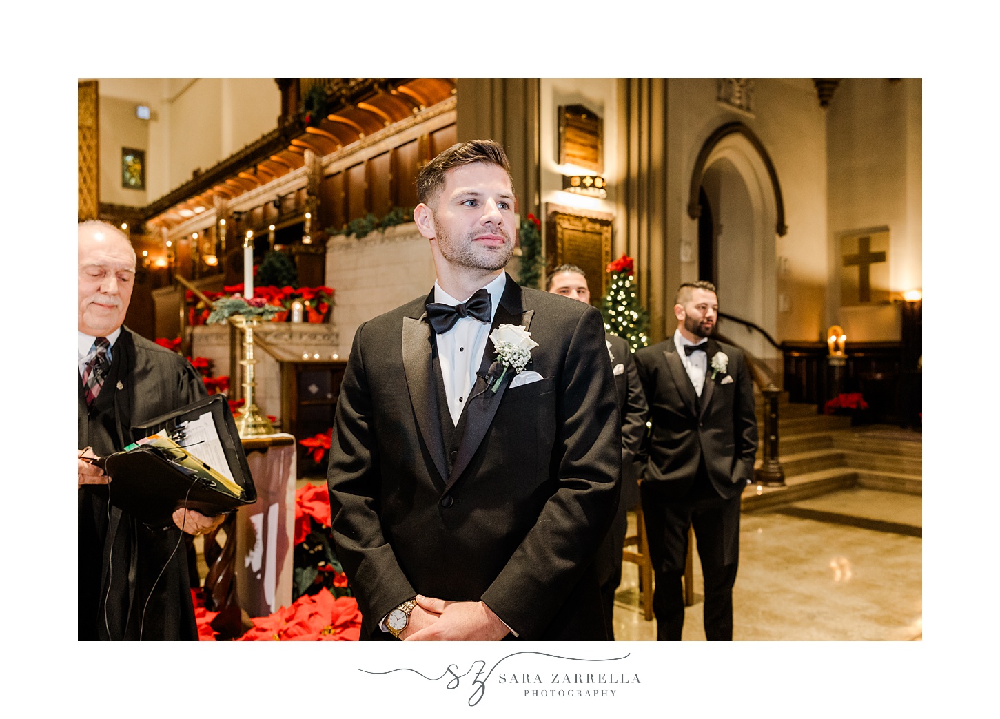 groom in black suit with white boutonniere turns to look down aisle
