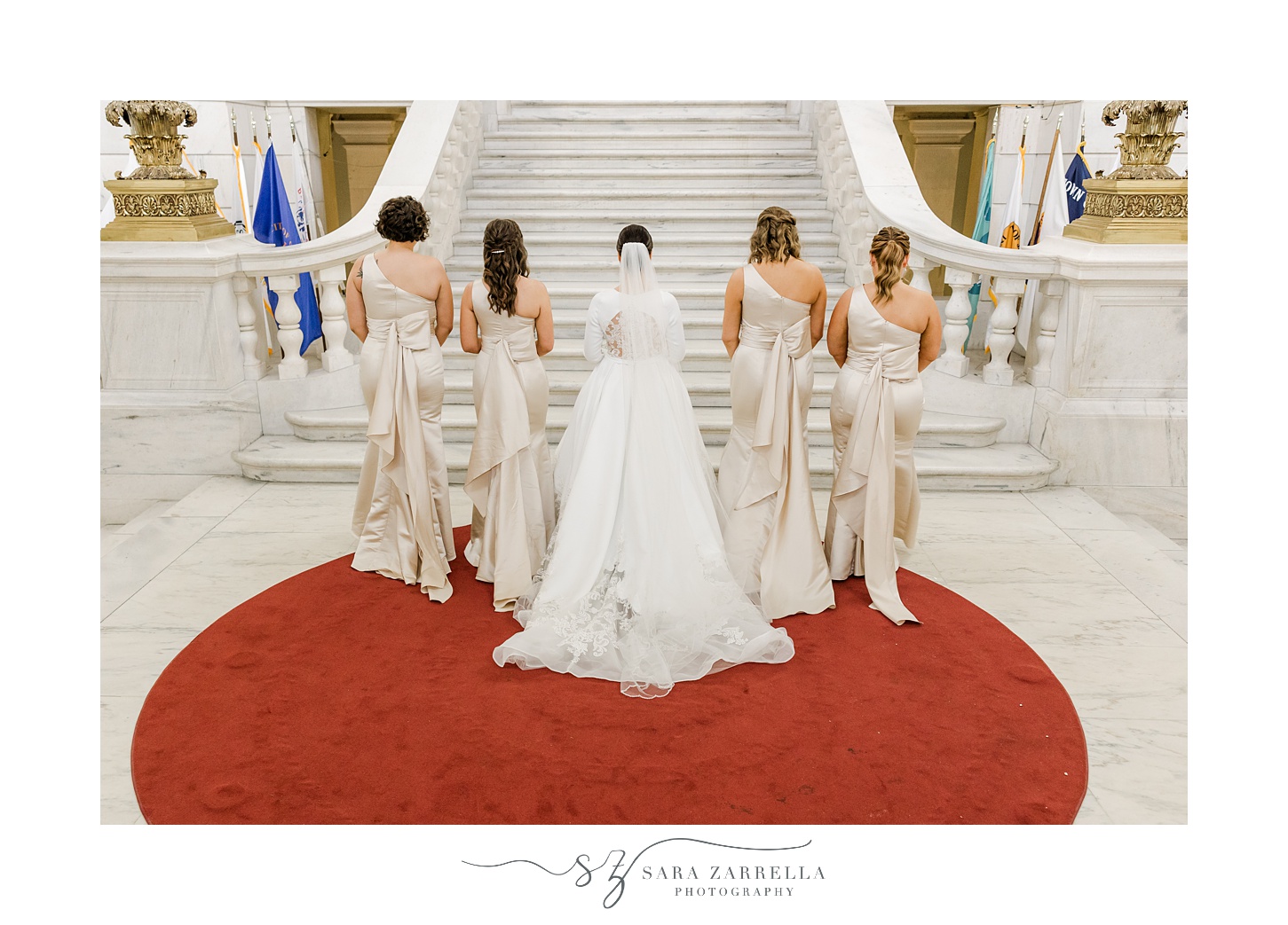 bride walks with bridesmaids in ivory gowns toward steps inside the Rhode Island State House in Providence RI