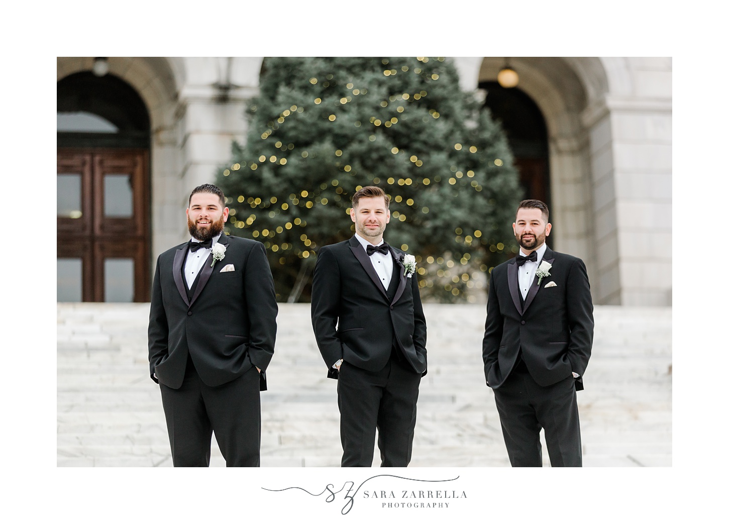 groom stands with groomsmen on steps near Christmas tree