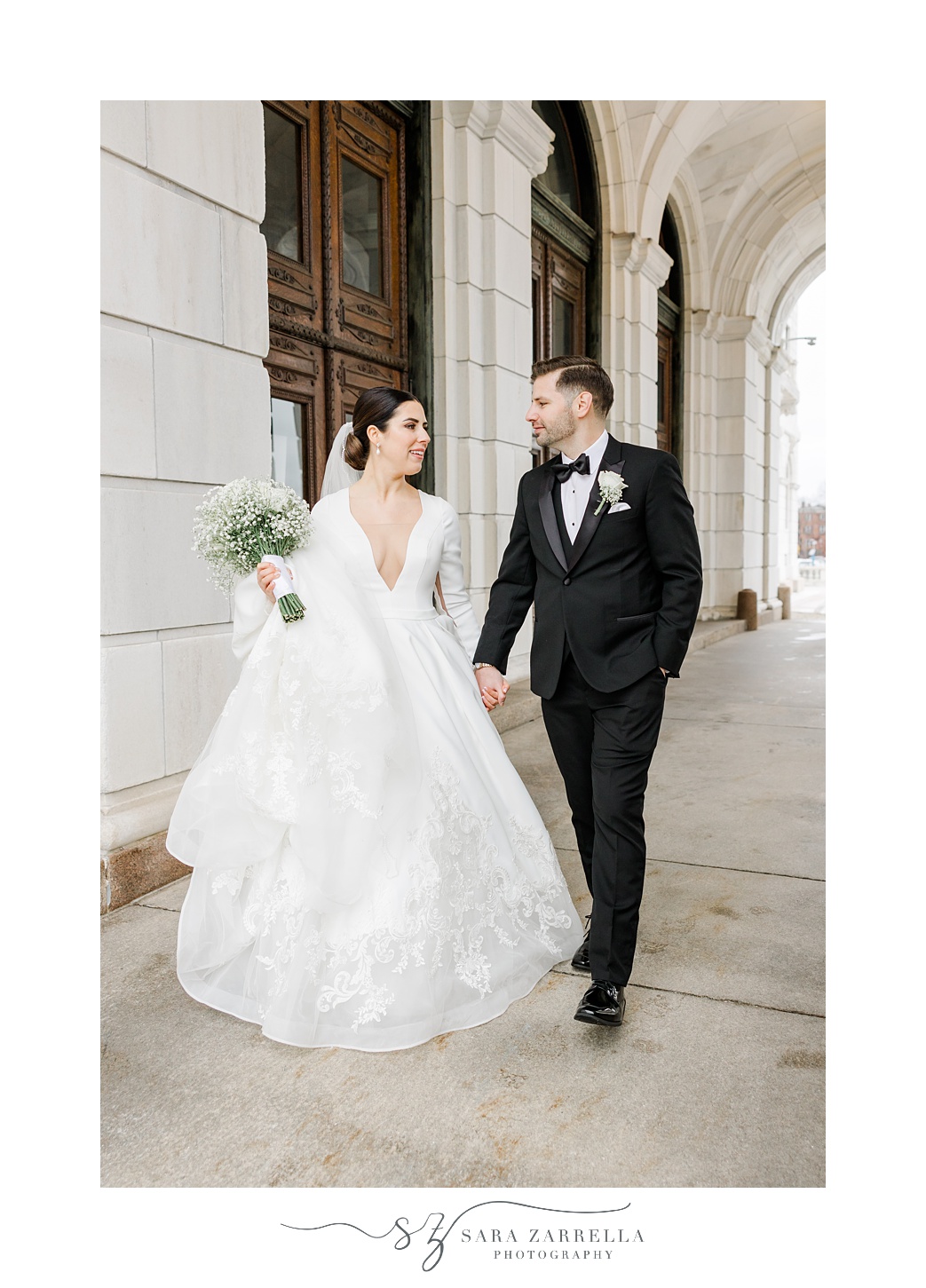 bride and groom hold hands walking down outside hallway of the Rhode Island State House in Providence RI