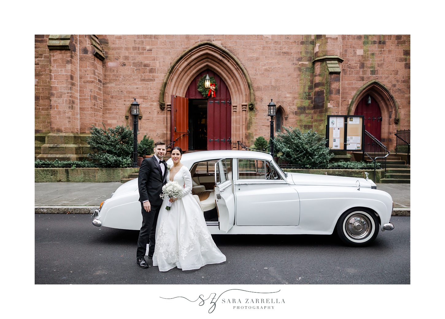 newlyweds hug by white classic car outside Providence RI church