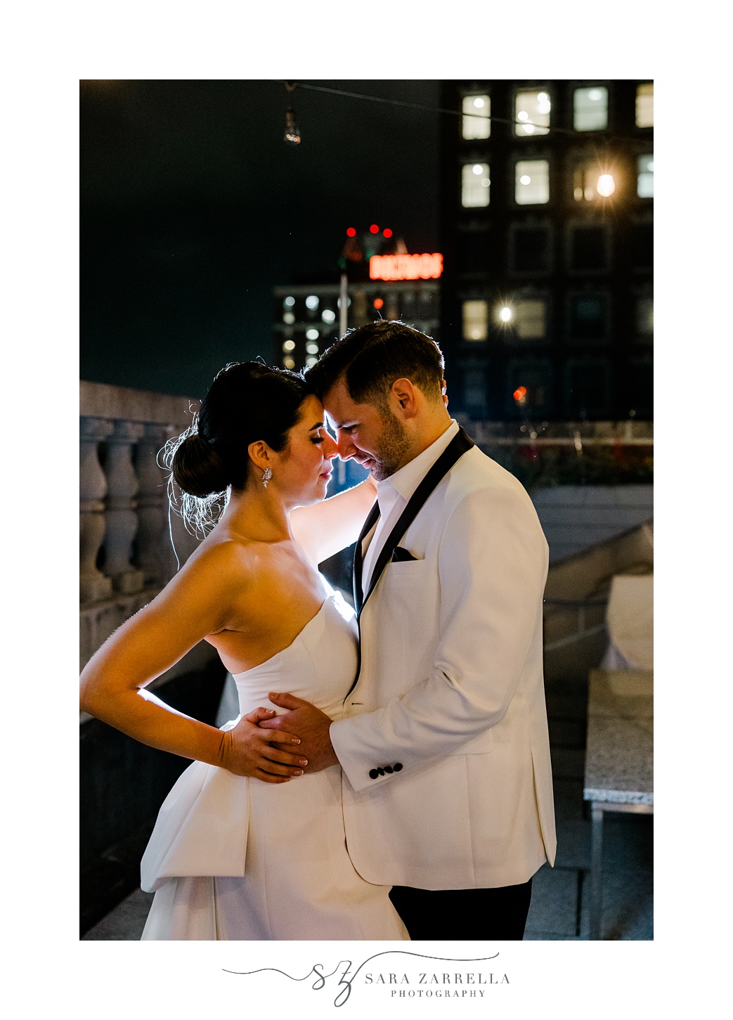 groom in white suit jacket with black lapels hugs bride in short white dress on rooftop of Providence G