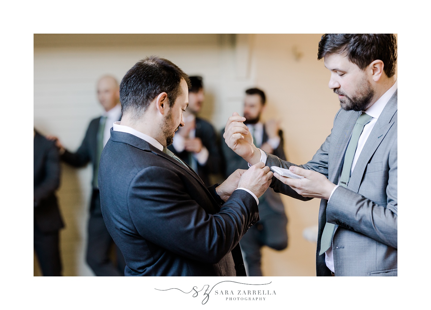groomsman helps groom with cufflinks on grey suit