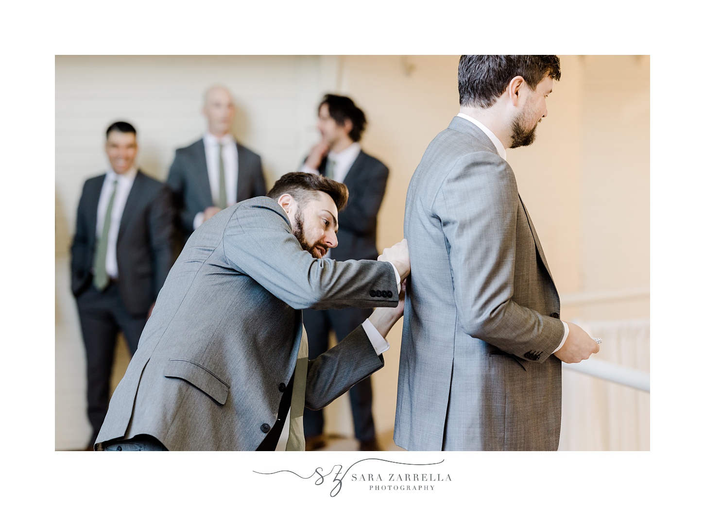 groomsman helps groom adjust suit jacket before RI wedding