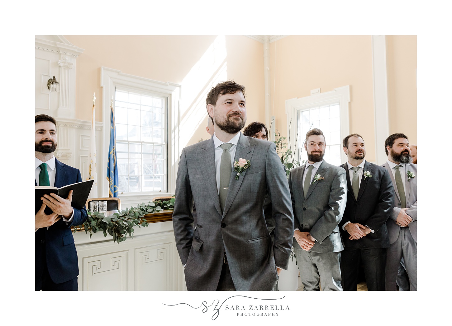 groom stands with hands in pockets of suit watching bride