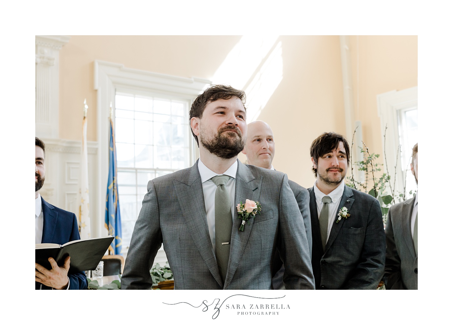 groom in grey suit smiles at bride during ceremony in East Greenwich