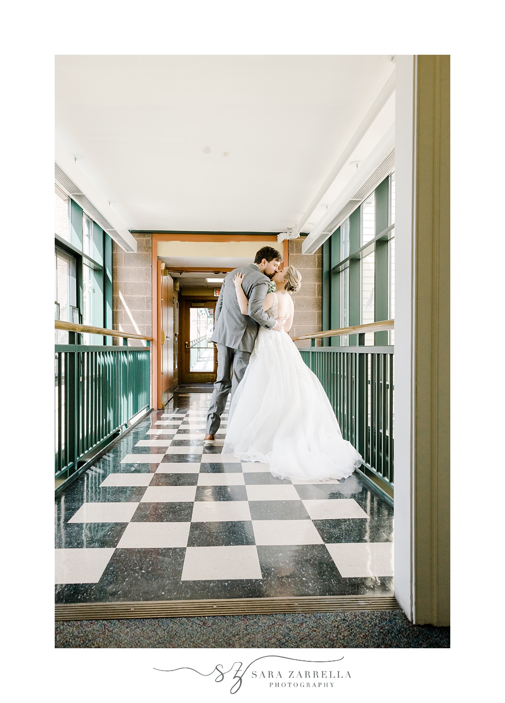bride and groom kiss in hallway with black and white floors and green railings at East Greenwich Town Hall