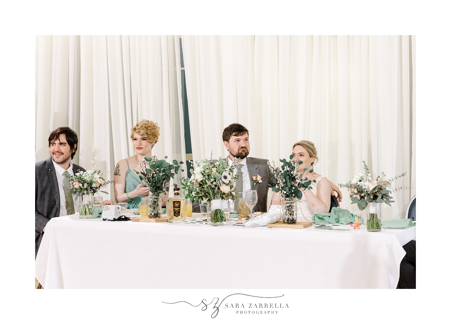 newlyweds sit with wedding party listening to toasts