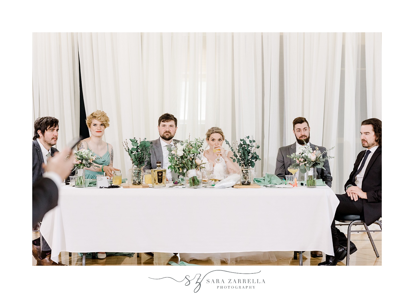 newlyweds sit with wedding party listening to toasts