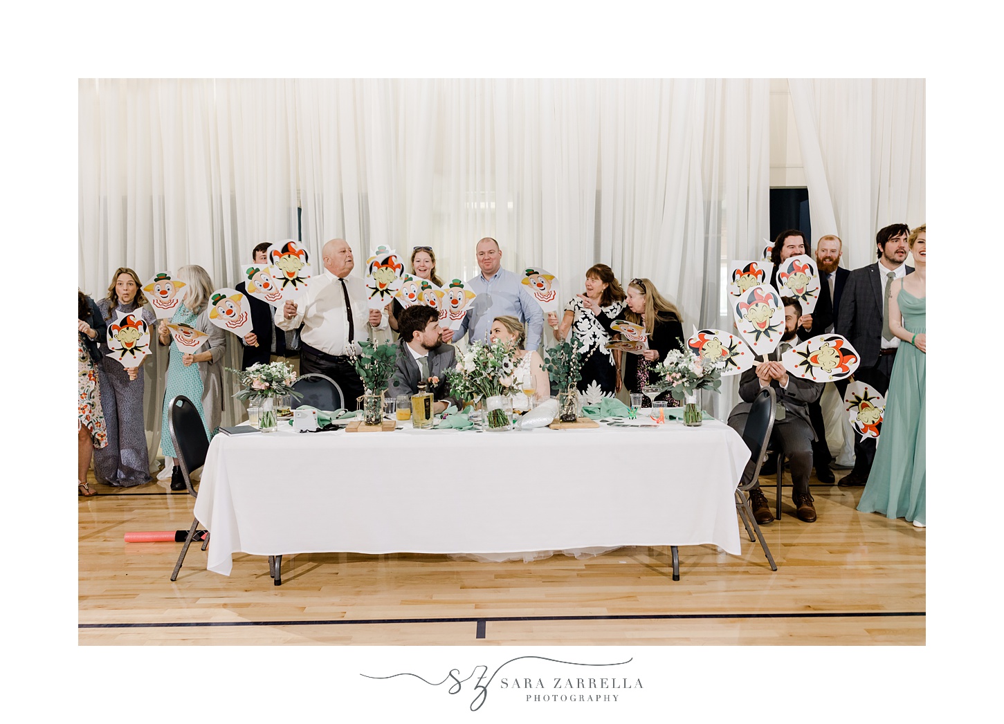 guests pose behind bride and groom holding up joker masks