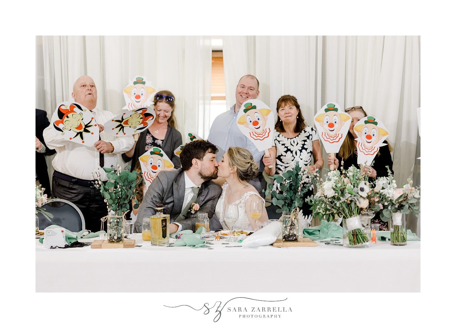 guests pose behind bride and groom holding up joker masks