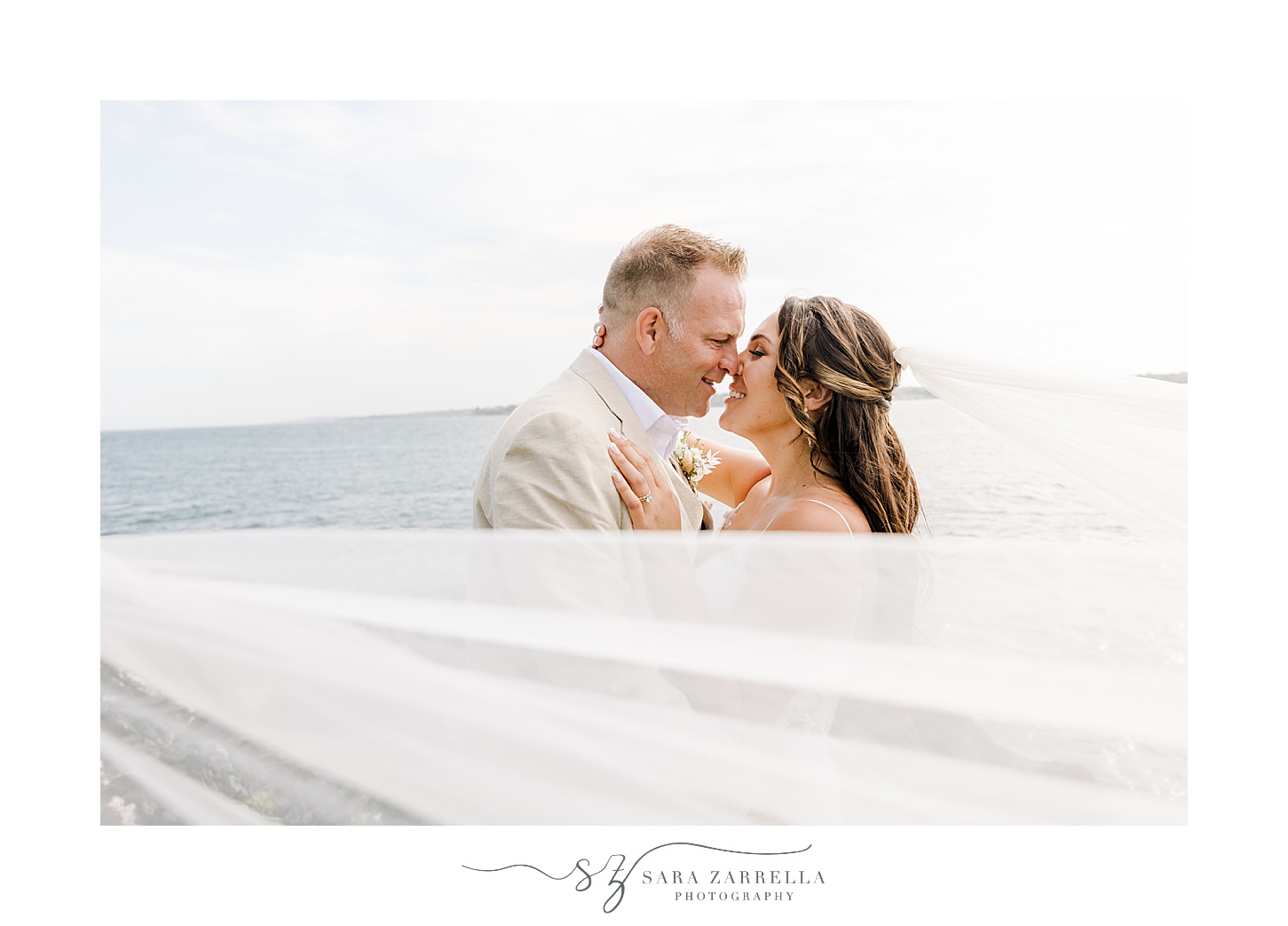 newlyweds lean to kiss with veil around them on beach at Fort Getty