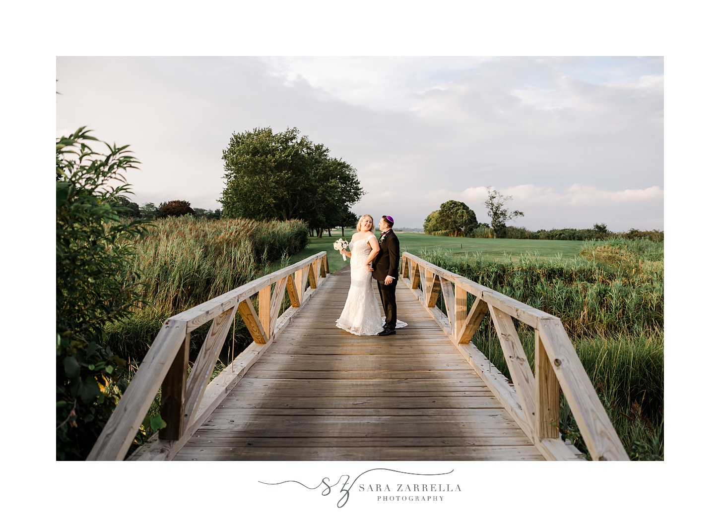 bride and groom stand on wooden bridge at sunset at Quidnessett Country Club