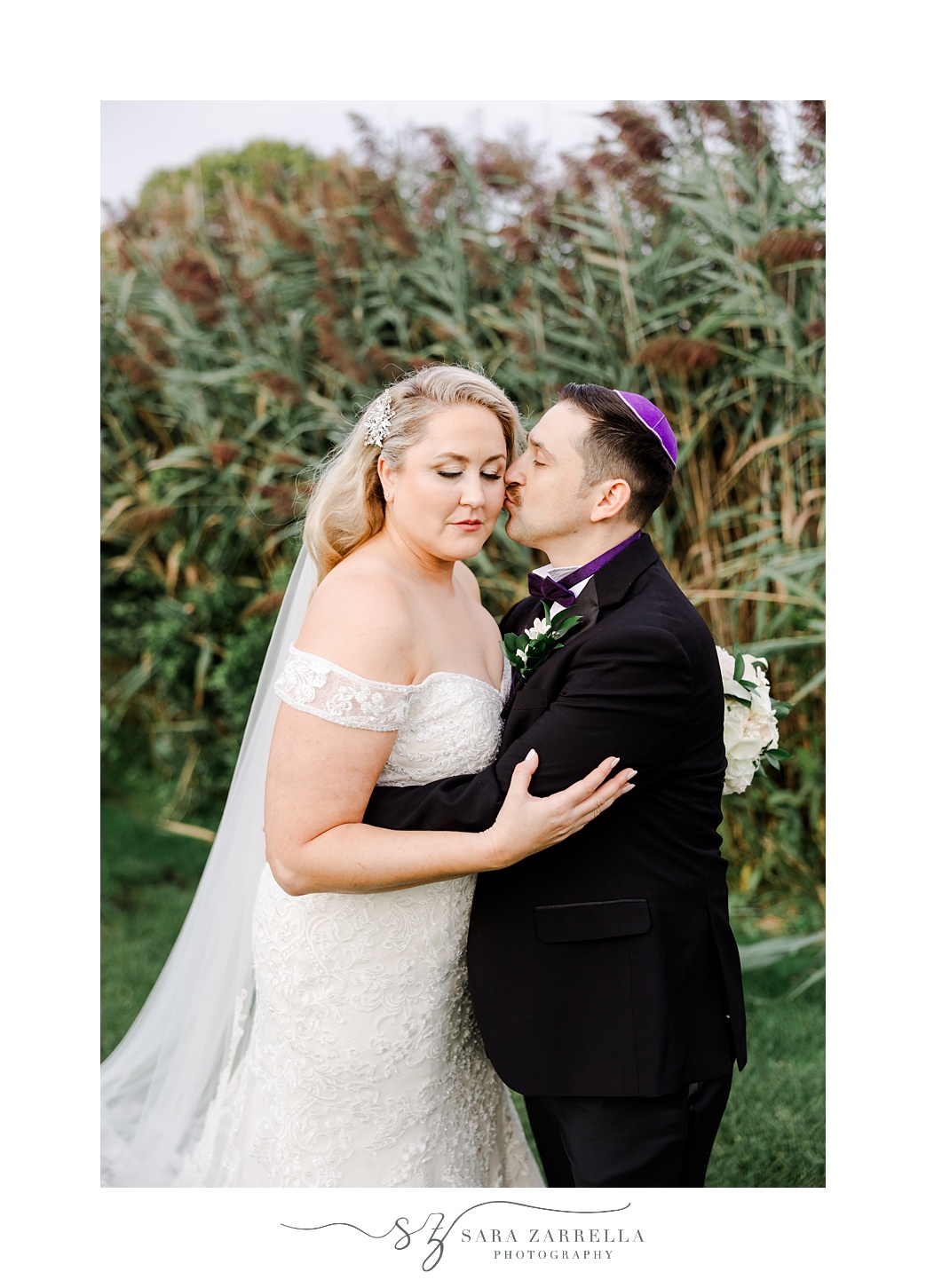 groom kisses bride's cheek during wedding portraits at Quidnessett Country Club