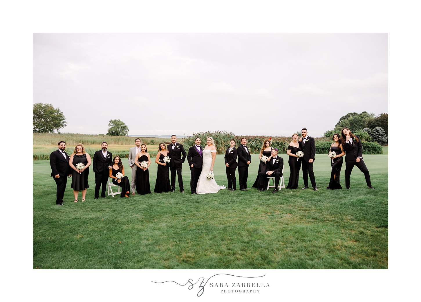 newlyweds stand on the lawn at Quidnessett Country Club with wedding party in black attire