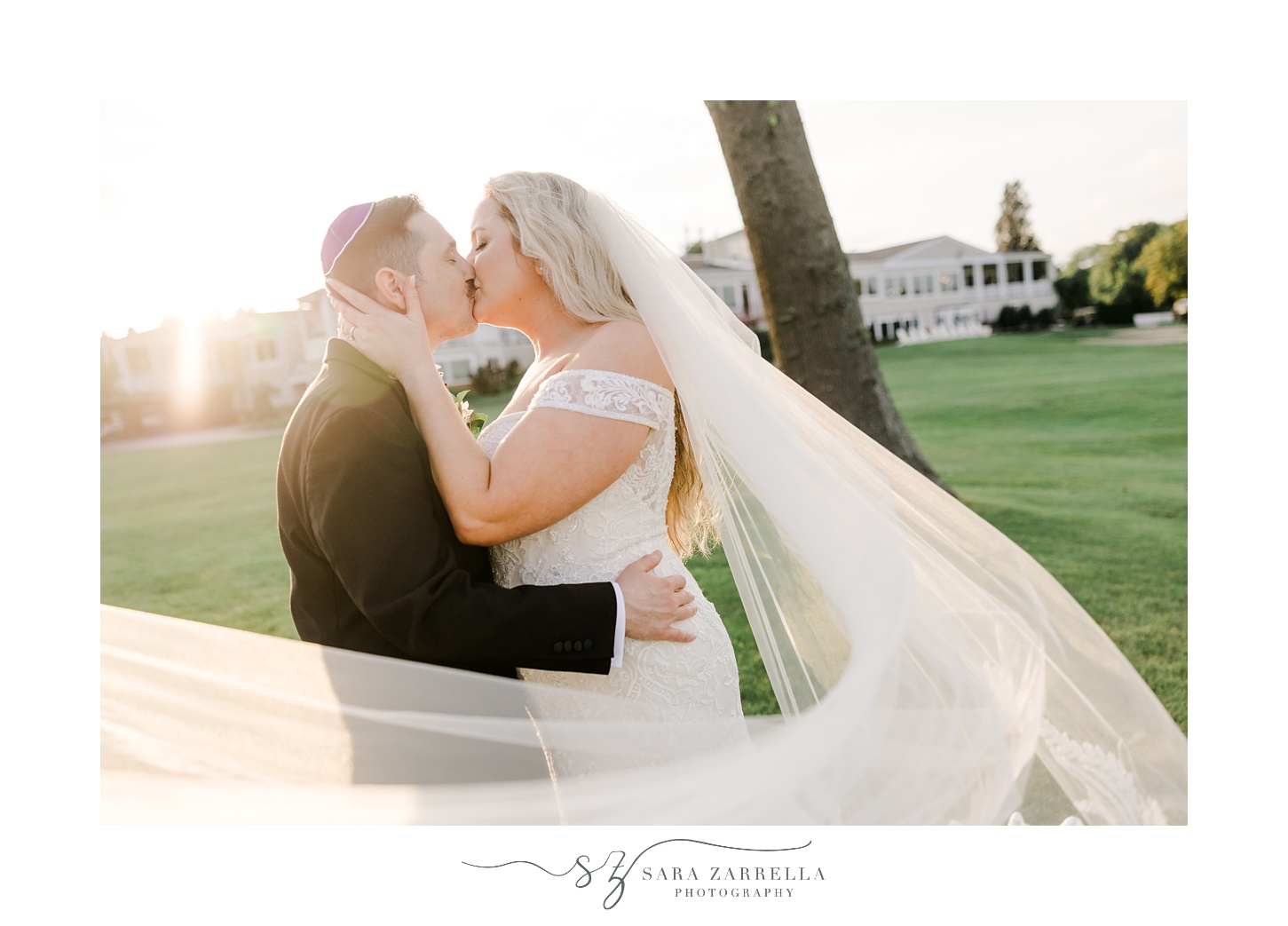 newlyweds kiss while bride's veil curls around them on the lawn at Quidnessett Country Club