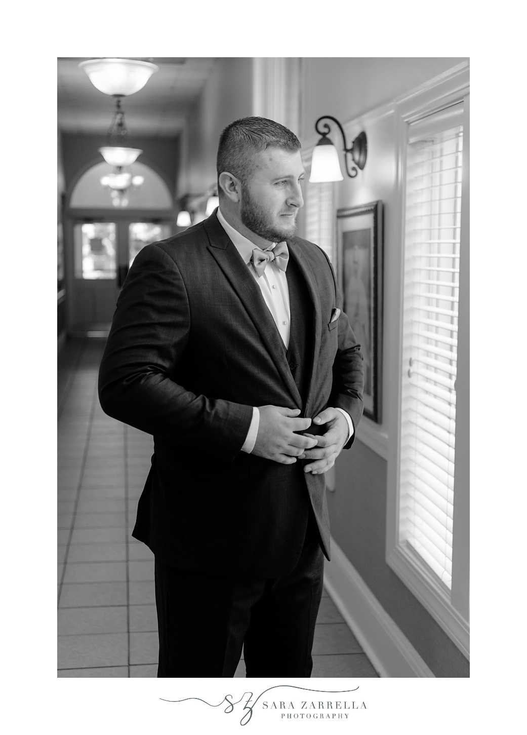 groom pulls suit jacket across chest in front of window