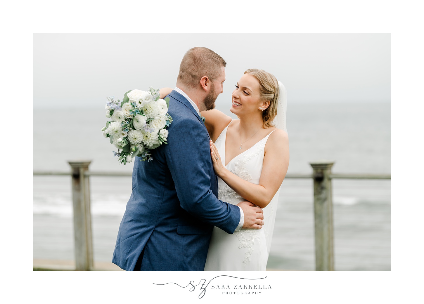 bride and groom hug each other smiling in front of Narragansett Bay