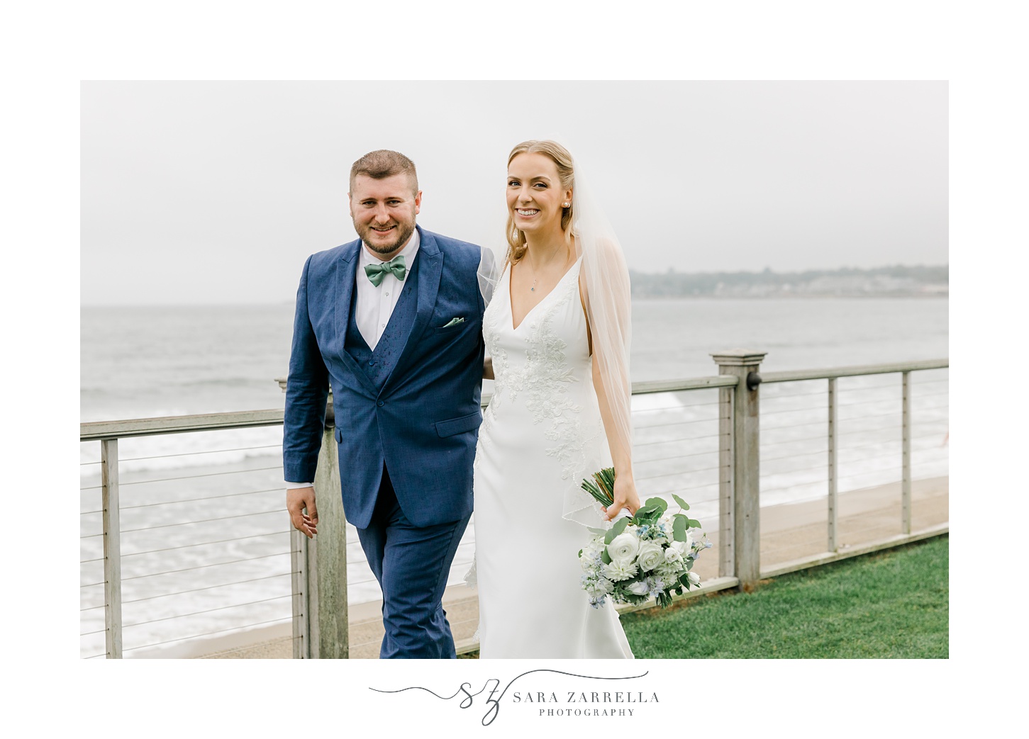 bride and groom laugh walking along railing near Narragansett Bay