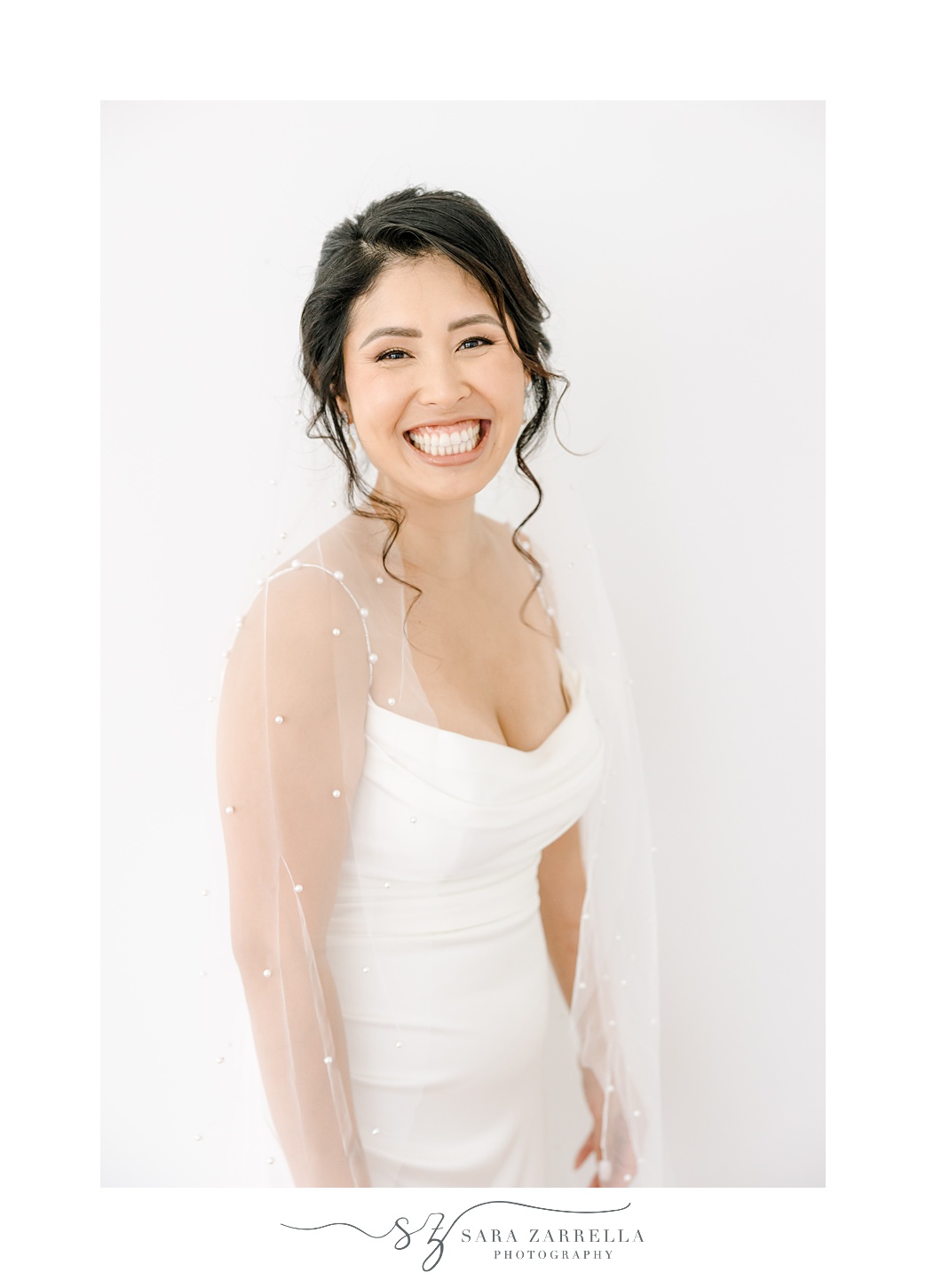 bride smiles in strapless wedding gown with veil around her shoulders