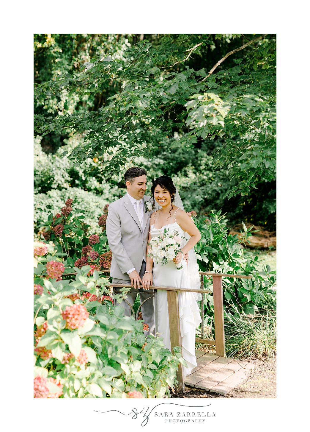 couple stands together on wooden wooden bridge in backyard garden