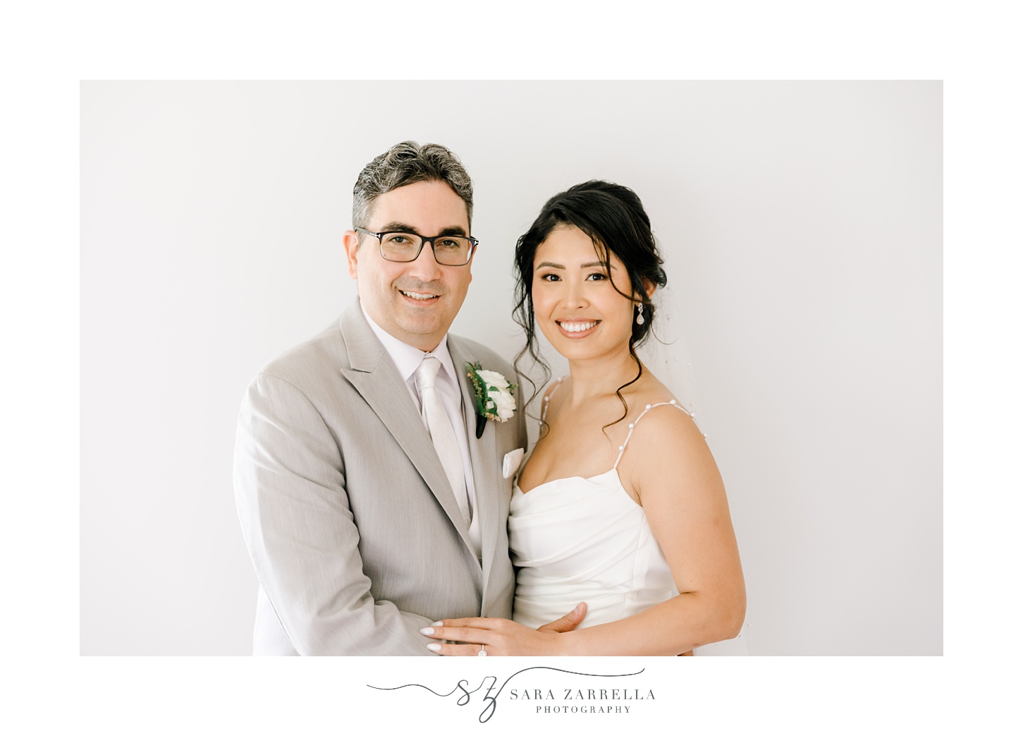 bride and groom hug smiling by white wall of home in Rhode Island