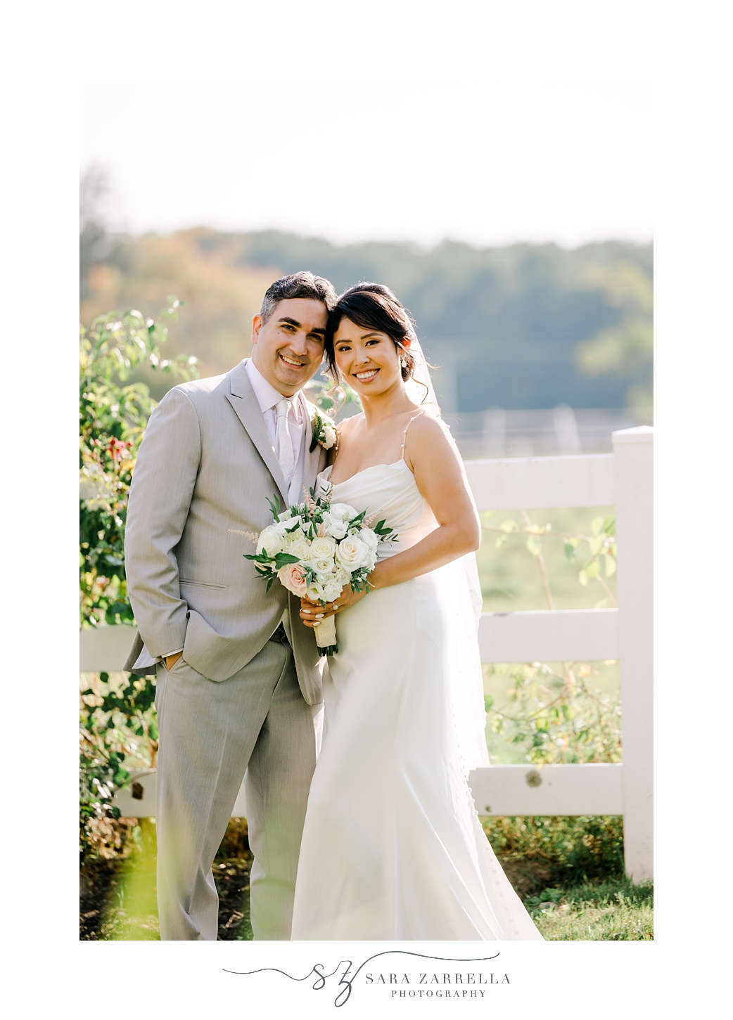 newlyweds smile leaning heads together during portraits in garden of Cranston RI home