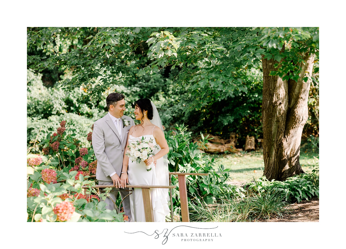 bride and groom stand on wooden bridge in backyard garden