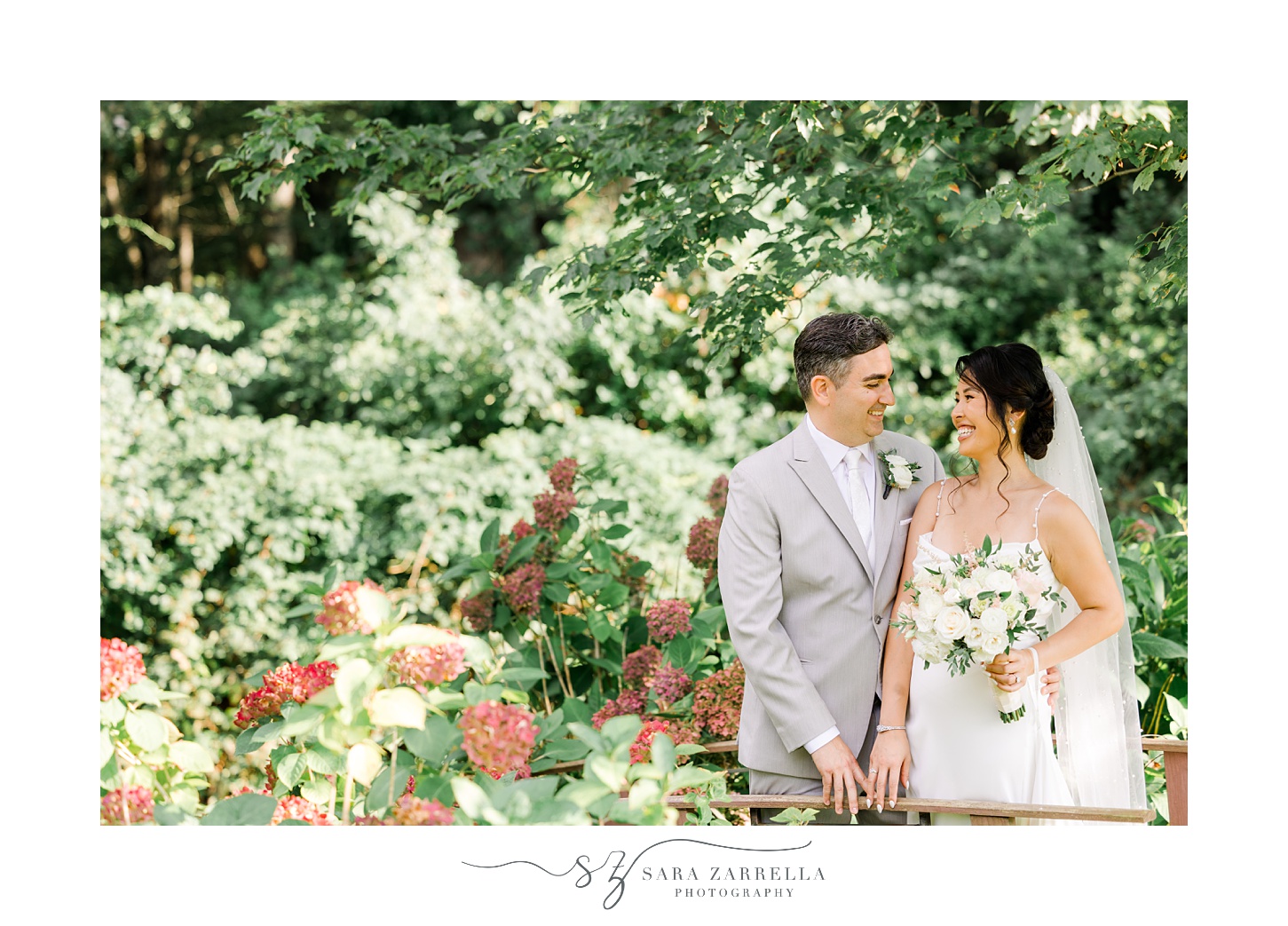 bride and groom look at each other standing on wooden wooden bridge in backyard garden