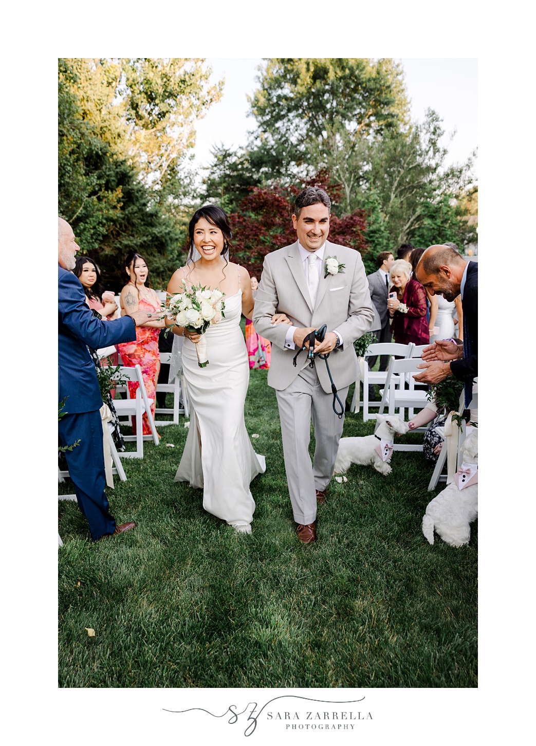 bride and groom walk dogs on leash up aisle after backyard wedding ceremony in Cranston RI