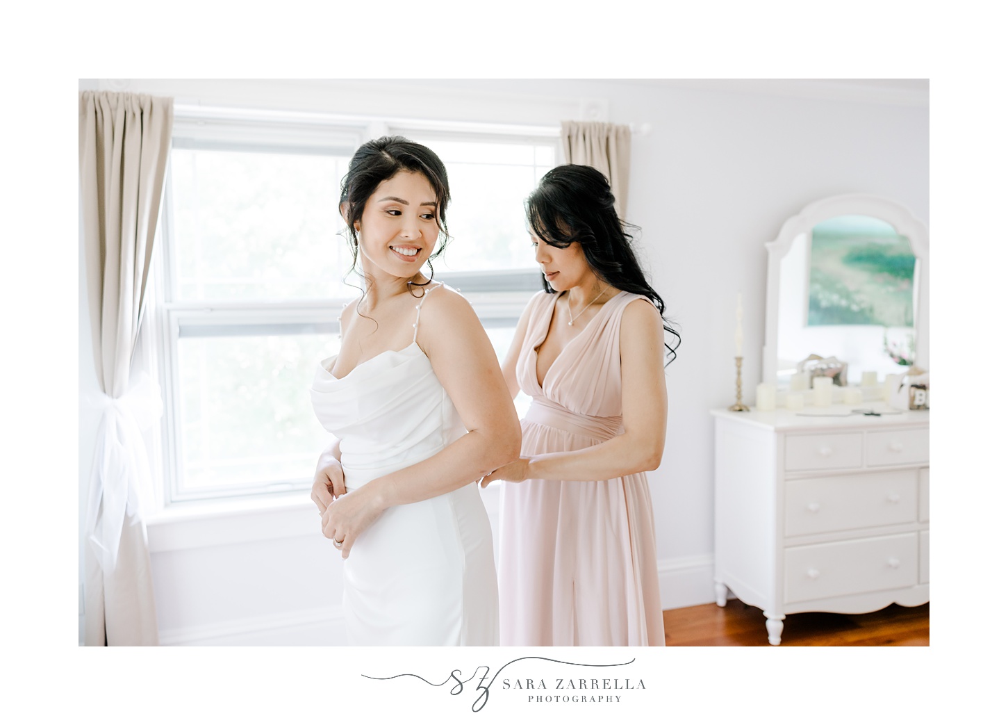 woman in pink dress helps bride with wedding gown in Cranston RI home