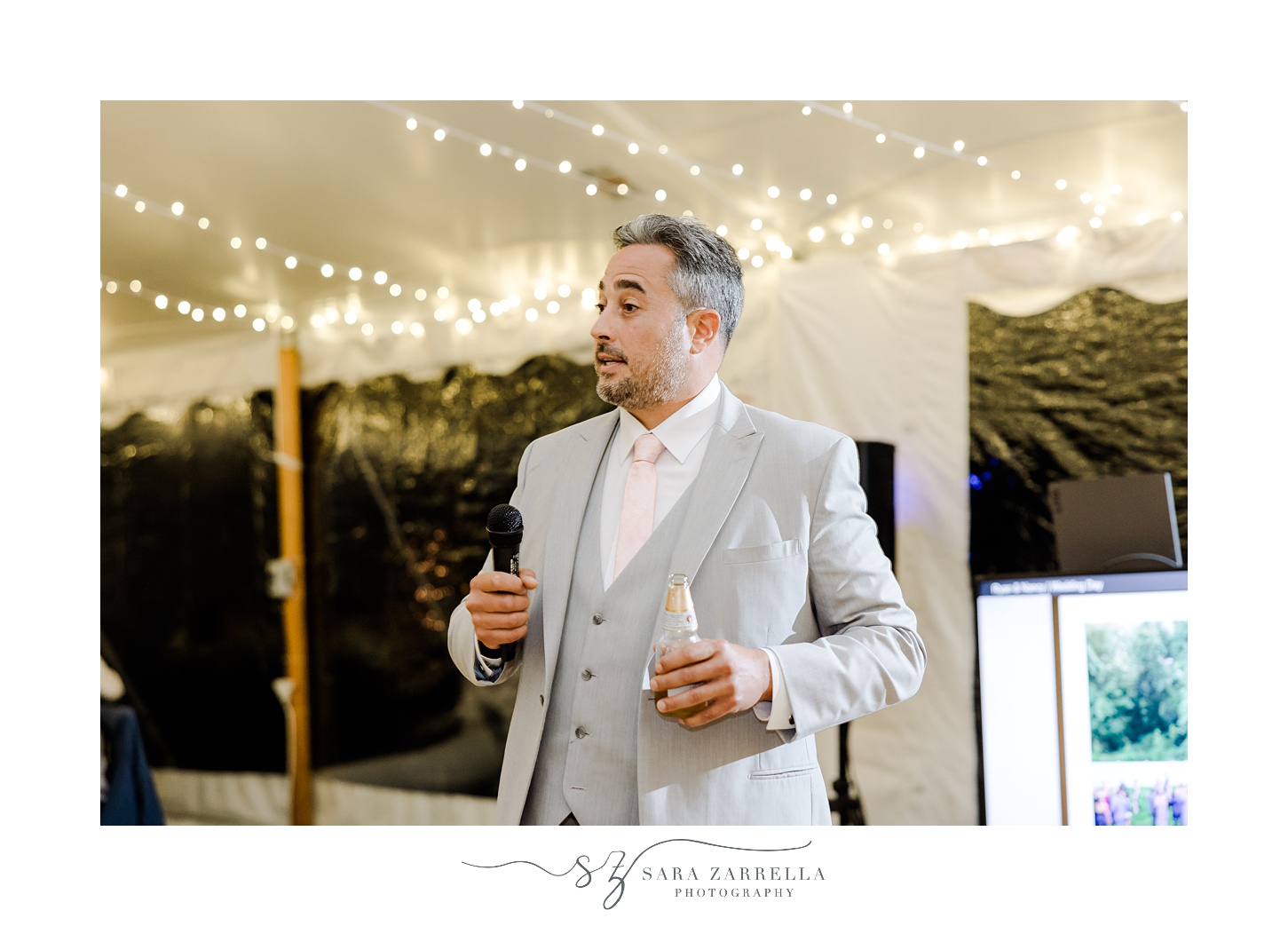 man in grey suit gives speech during tented reception for backyard wedding in Cranston RI