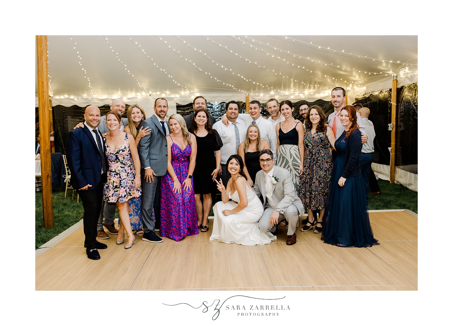 bride and groom pose with wedding guests on dance floor during tented reception for backyard wedding in Cranston RI