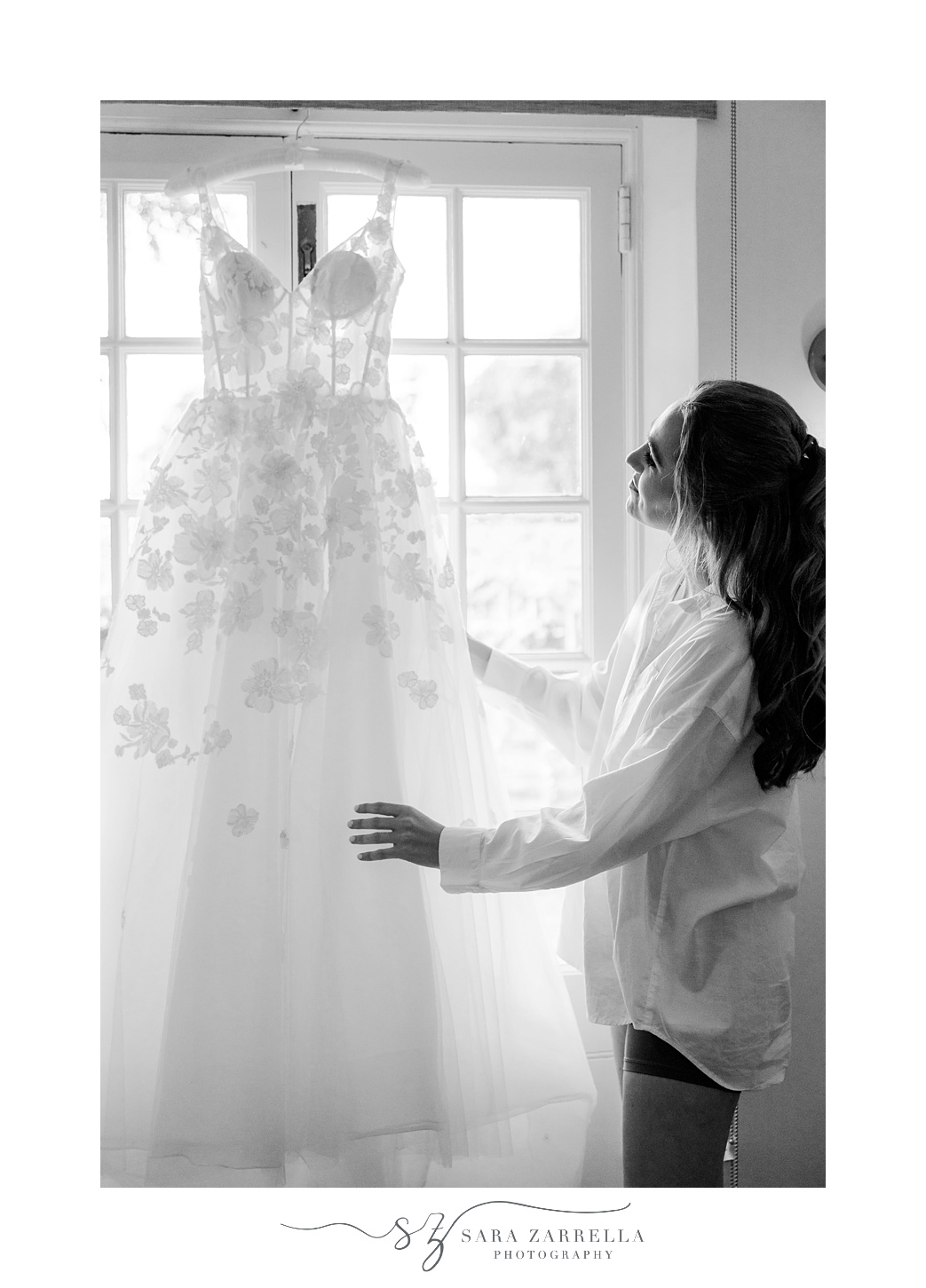 bride looks at wedding dress hanging in the window of suite at Shepard's Run