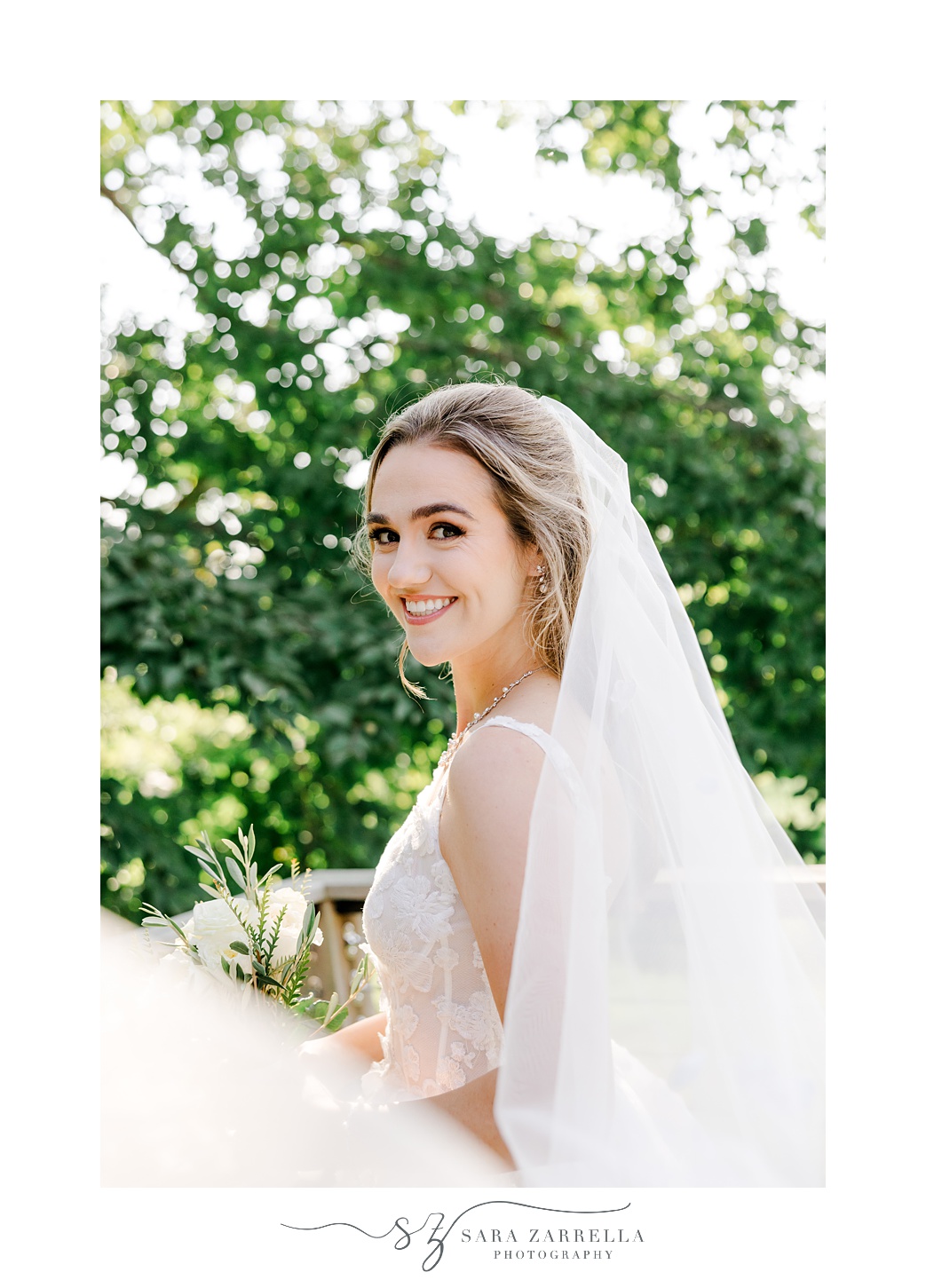 bride smiles over her shoulder with veil pulled out around her
