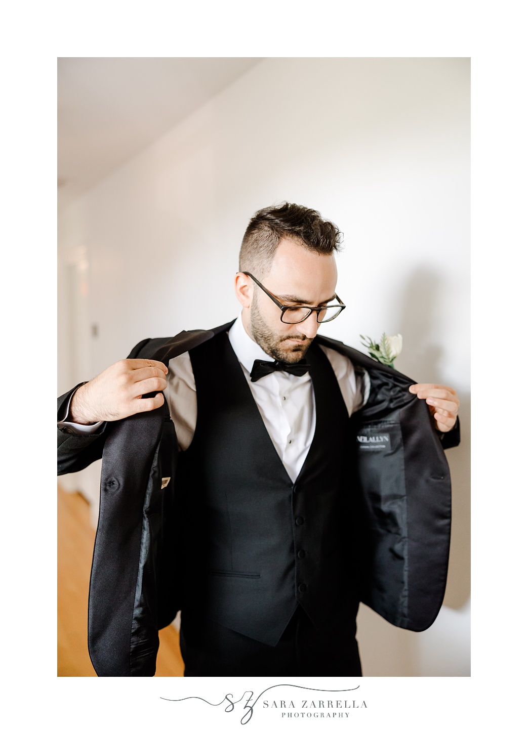 groom pulls on suit jacket while preparing for Rhode Island wedding