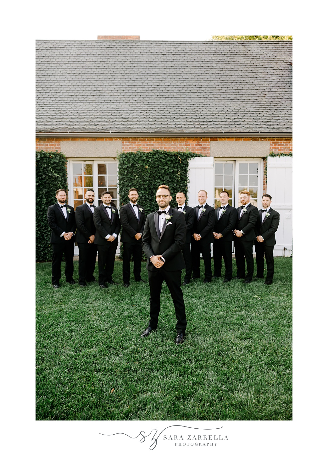 groom stands with groomsmen behind him by small house on land at Shepard's Run