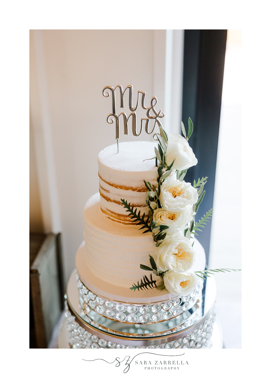 tiered naked wedding cake with white flowers on the side