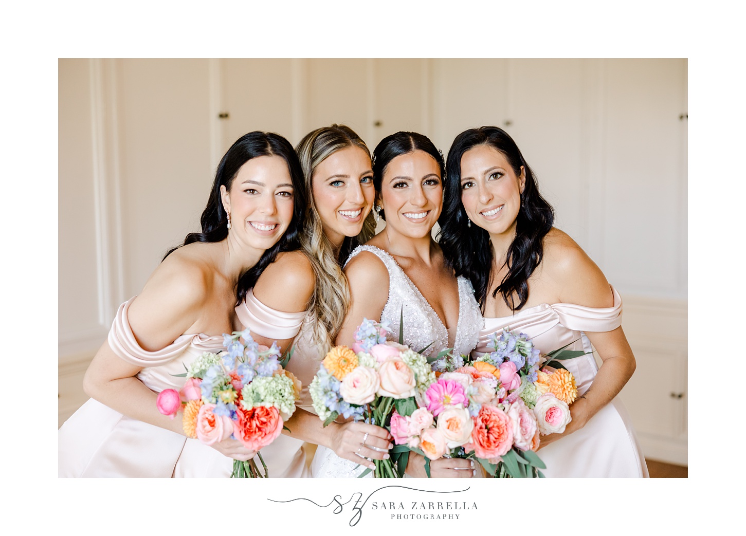 bride smiles hugging close with bridesmaids in light pink gowns with bright bouquets