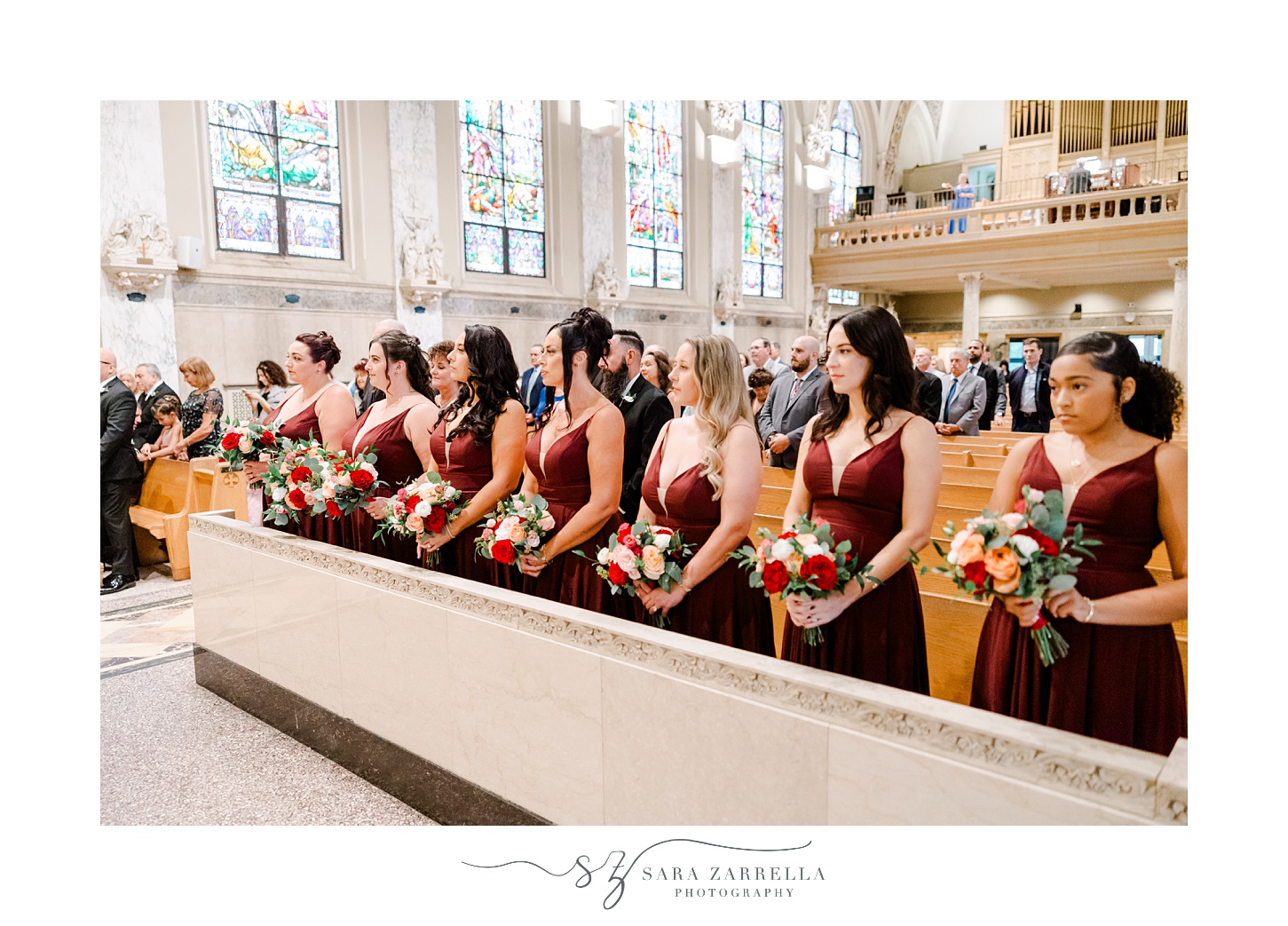bridesmaids in burgundy gowns stand holding bouquets inside the Holy Ghost Church