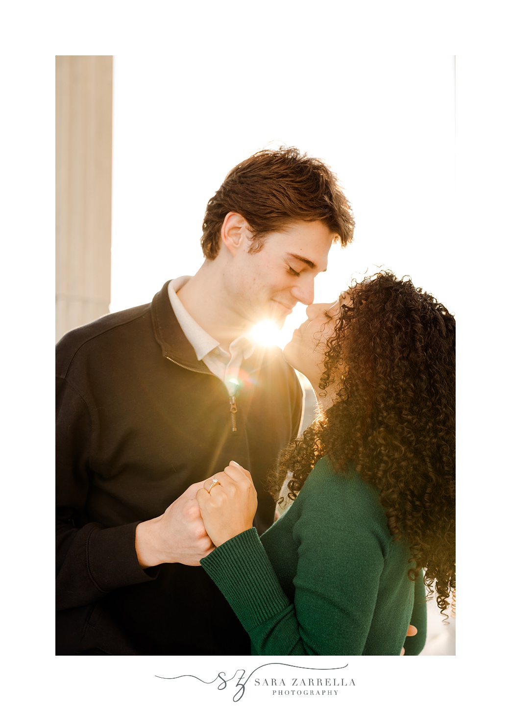 couple smiles with sun flare behind them in Rhode Island