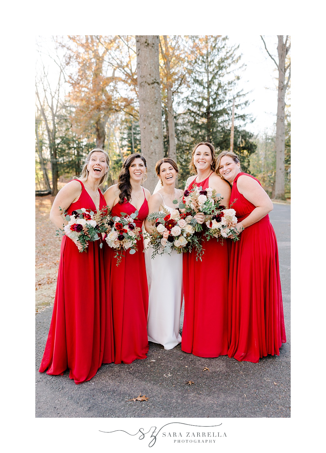 brides poses with bridesmaids in red gowns outside Quidnessett Country Club