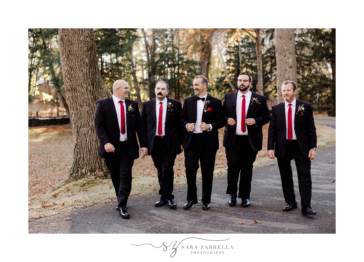 groom stands with groomsmen in black suits with red ties for fall wedding day